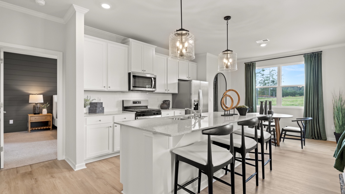 Modern kitchen with bright natural lighting, white cabinetry, stainless steel appliances, and an island with a sink