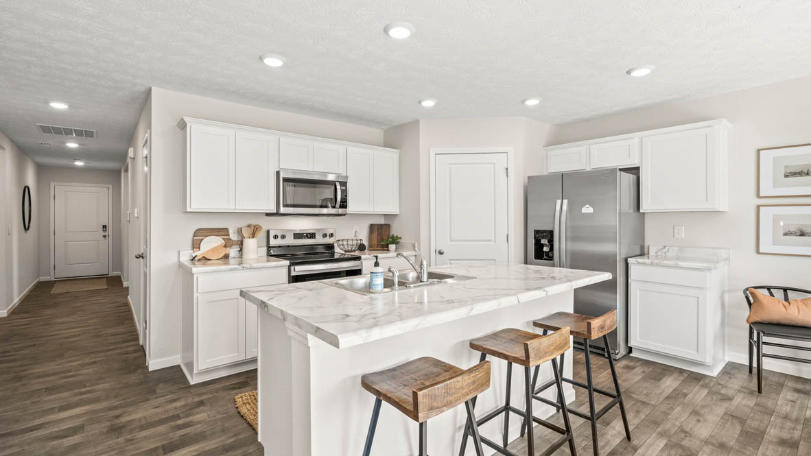 Full view of kitchen with white cabinets and hallway to front door.