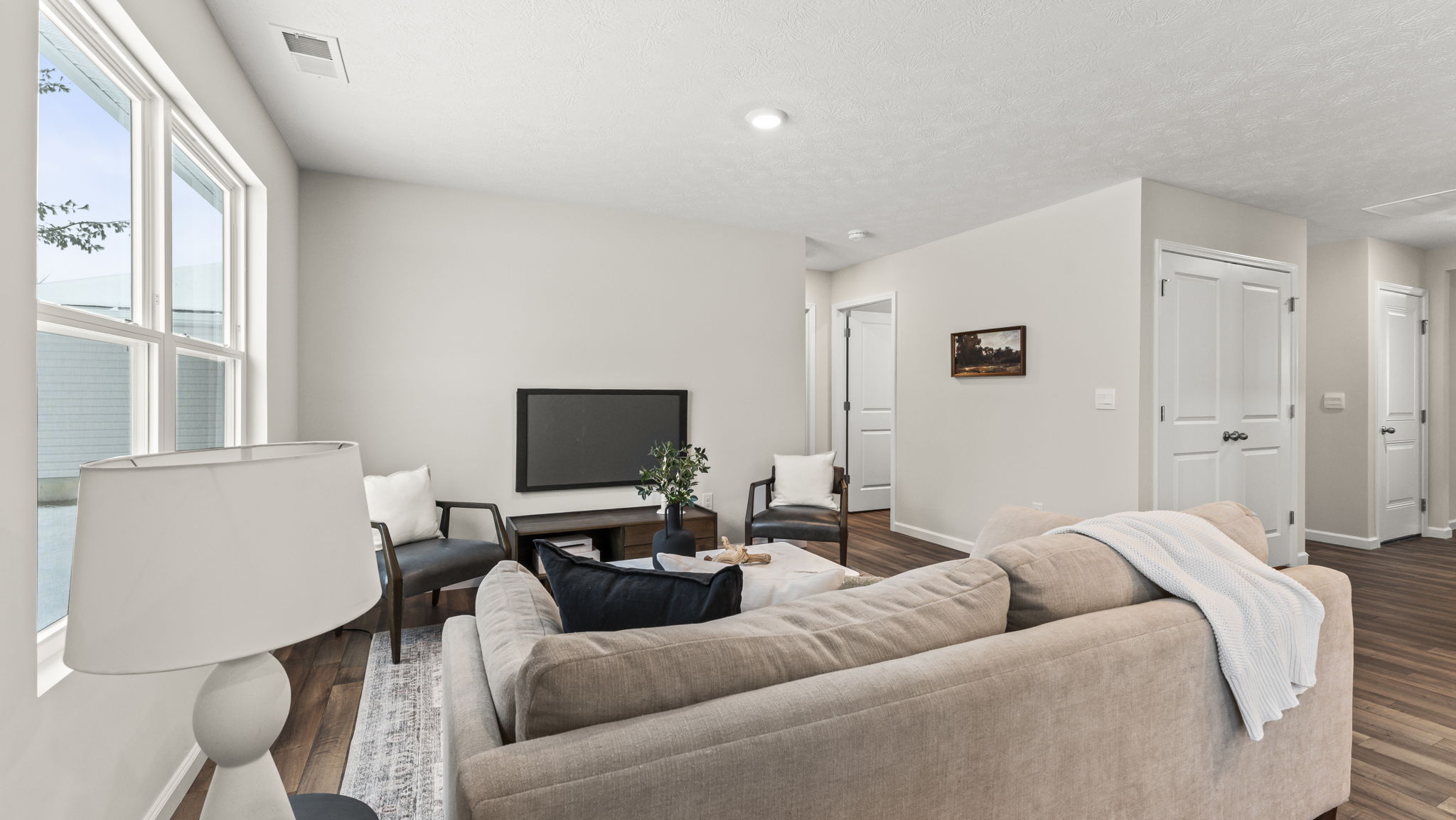 Main-level living room with bright windows and open flow to kitchen, dining, and backyard