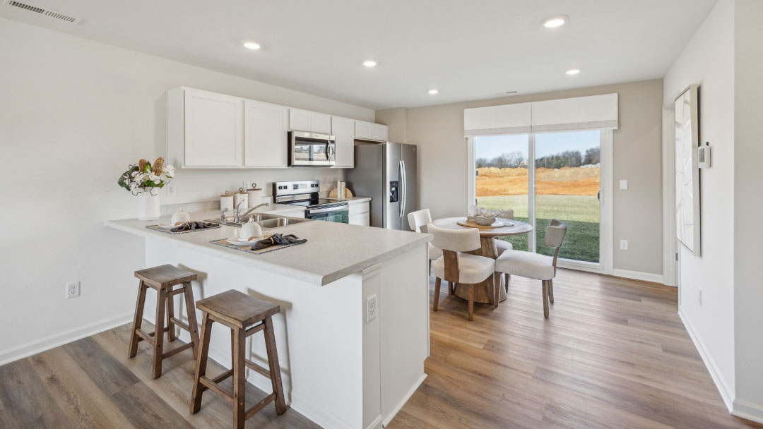 modern kitchen with white cabinetry, stainless steel appliances, 2 counter stools, and a large sliding door to the backyard