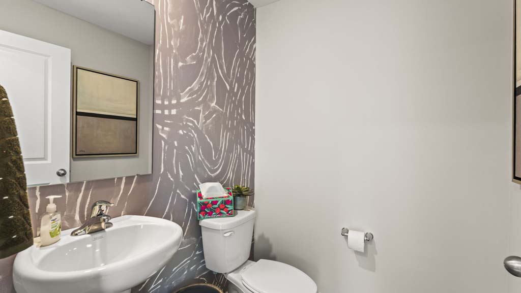 Bathroom with earthy wallpaper, mirror, sink, and toilet