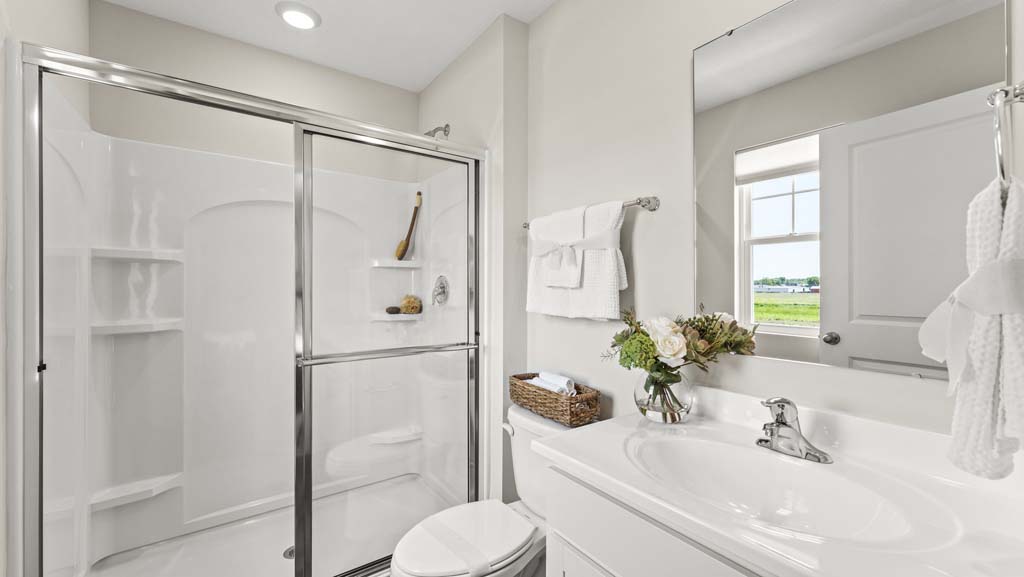 Clean white primary bathroom with walk-in shower, toilet, sink, and mirror