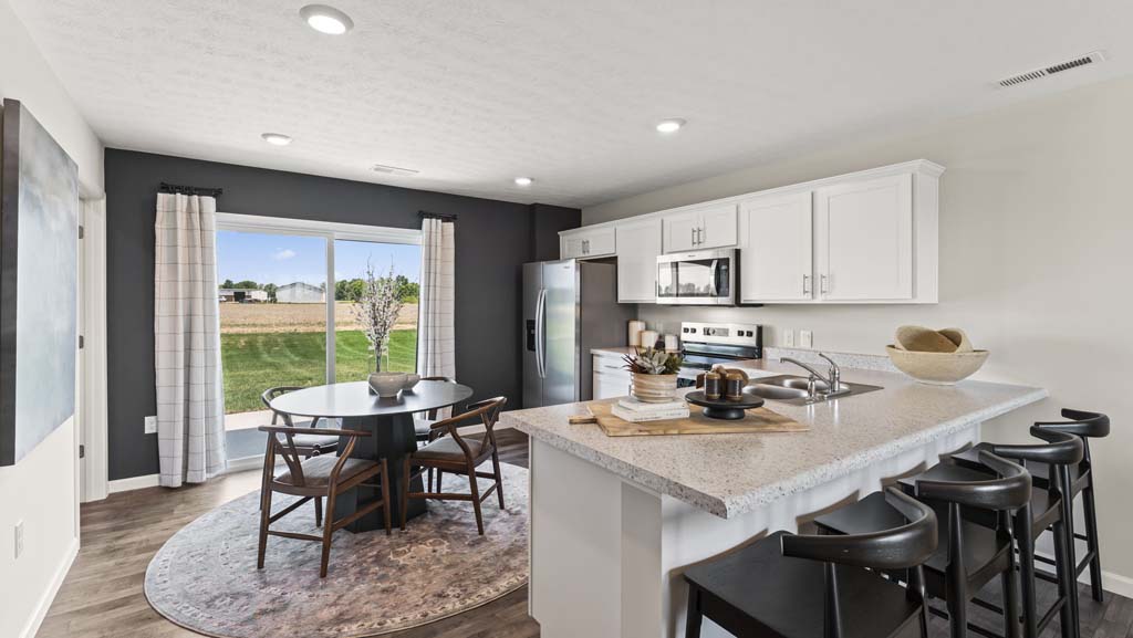 Wide angle of kitchen with laminate counters, chairs, kitchen table, stainless steel appliances, and white cabinetry