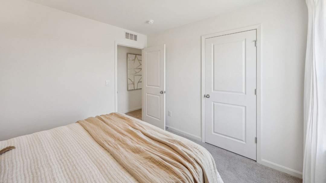 bedroom decorated in white and beige tones, featuring a bed and 2 wooden night stands on each side, with a window on the left wall of the bed