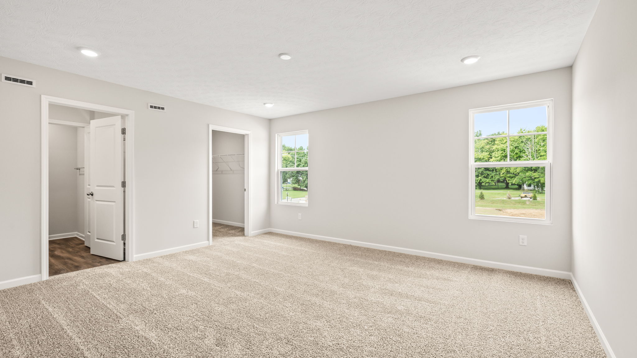 Carpeted primary bedroom with two windows, door to bathroom, and closet