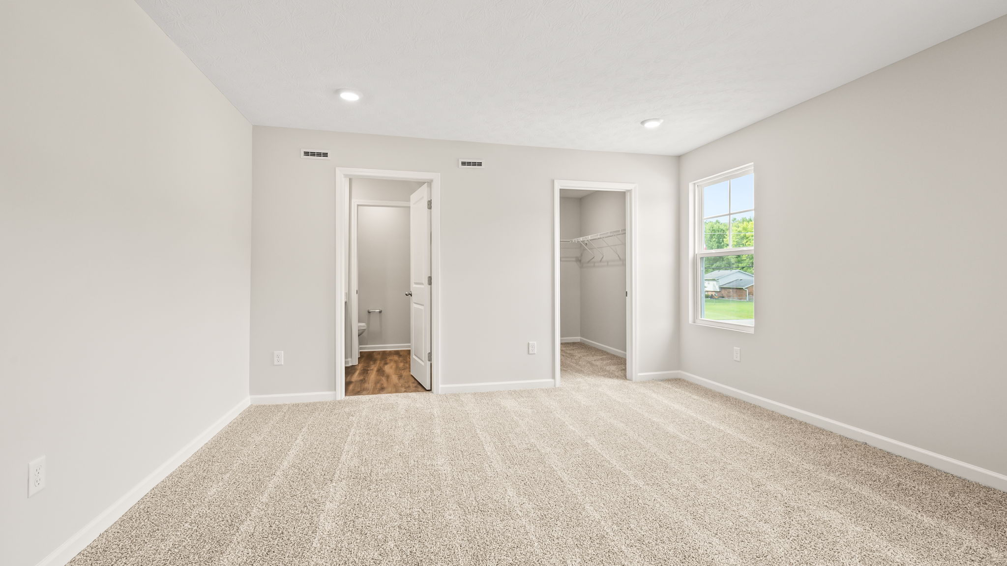 Carpeted primary bedroom with window, door to bathroom, and closet