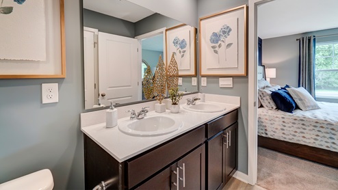 Dual vanity sinks in the primary bedroom with a large mirror and view into primary suite.