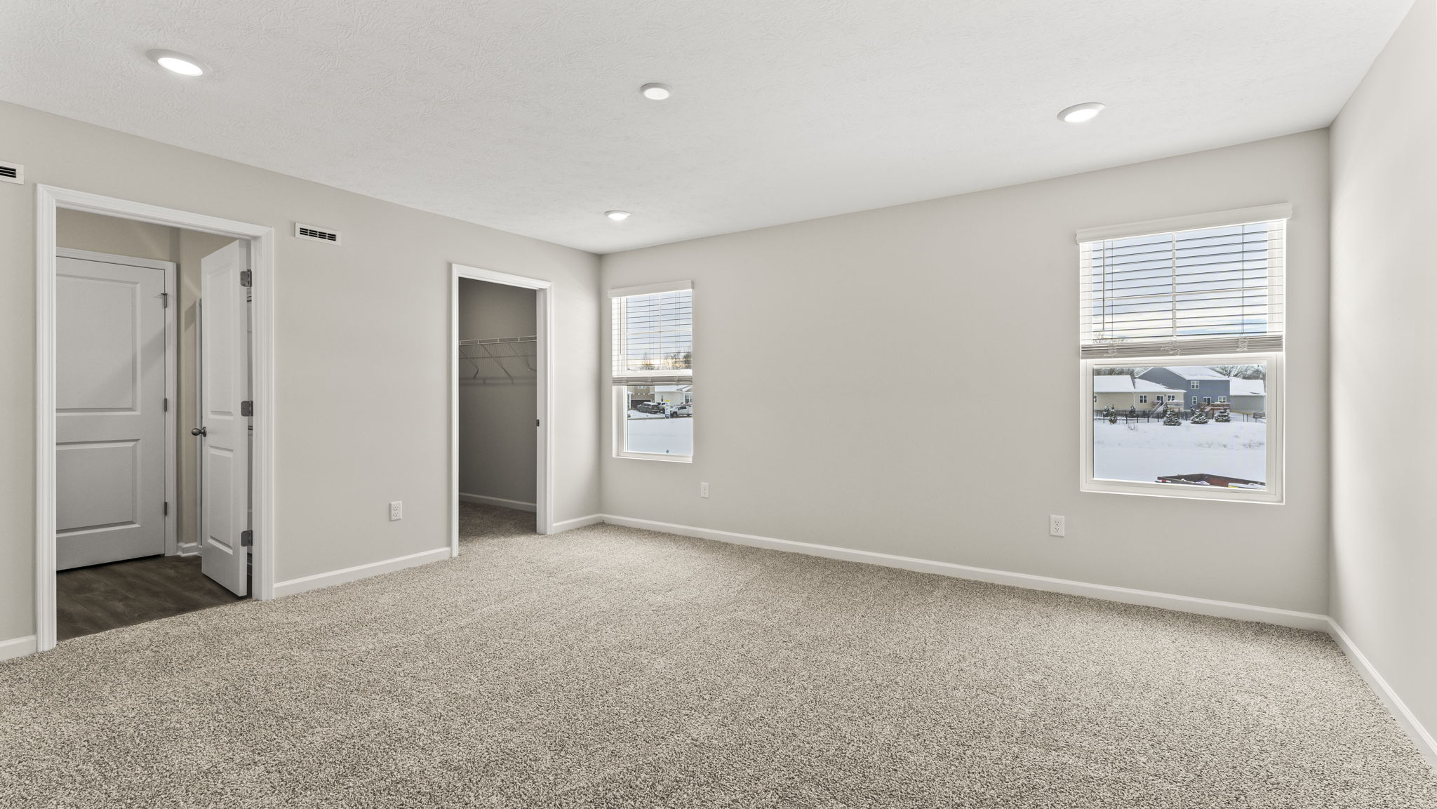 Primary bedroom with view of bathroom, walk-in closet, and windows
