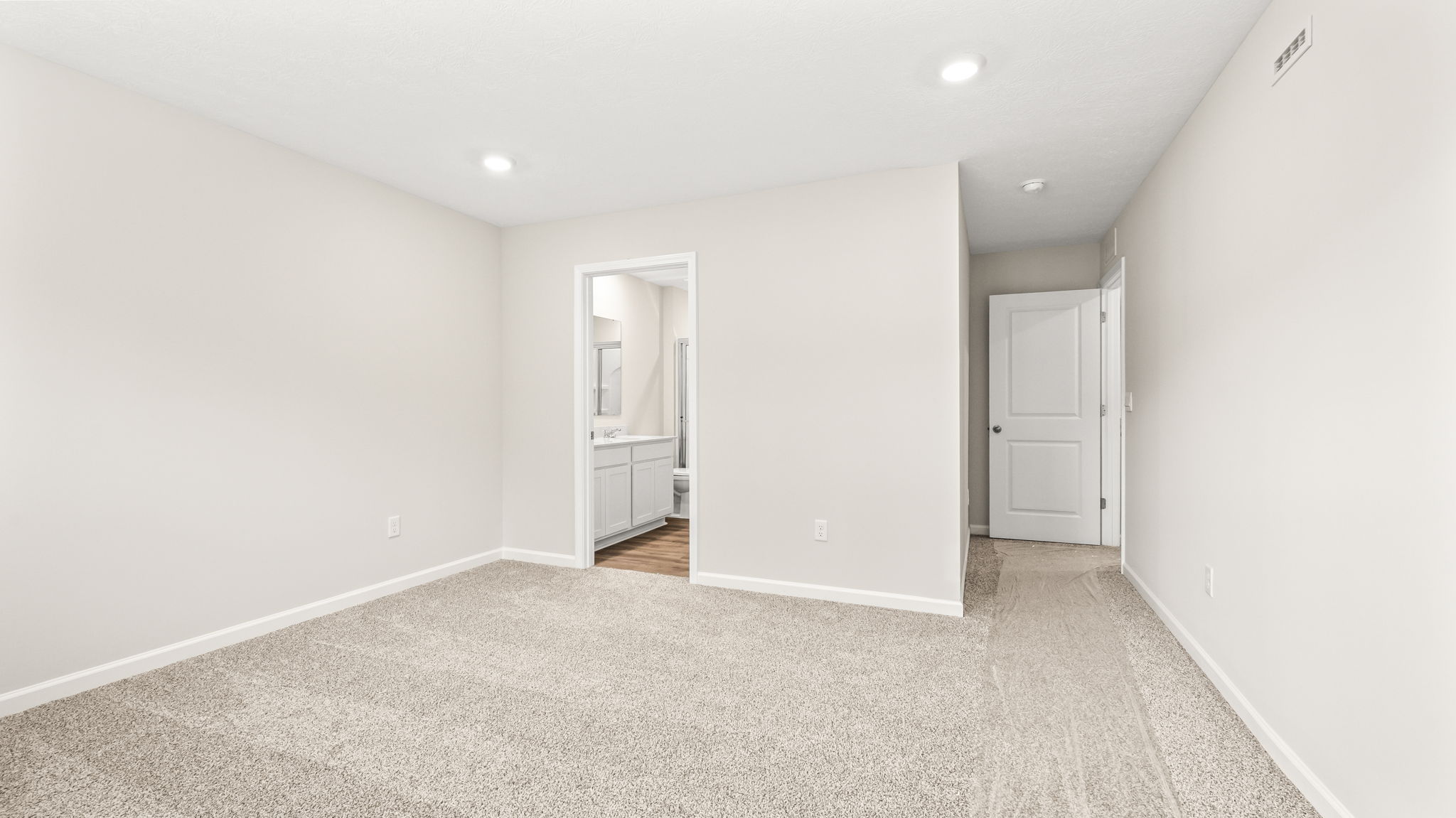 Carpeted primary bedroom with view of bathroom suite