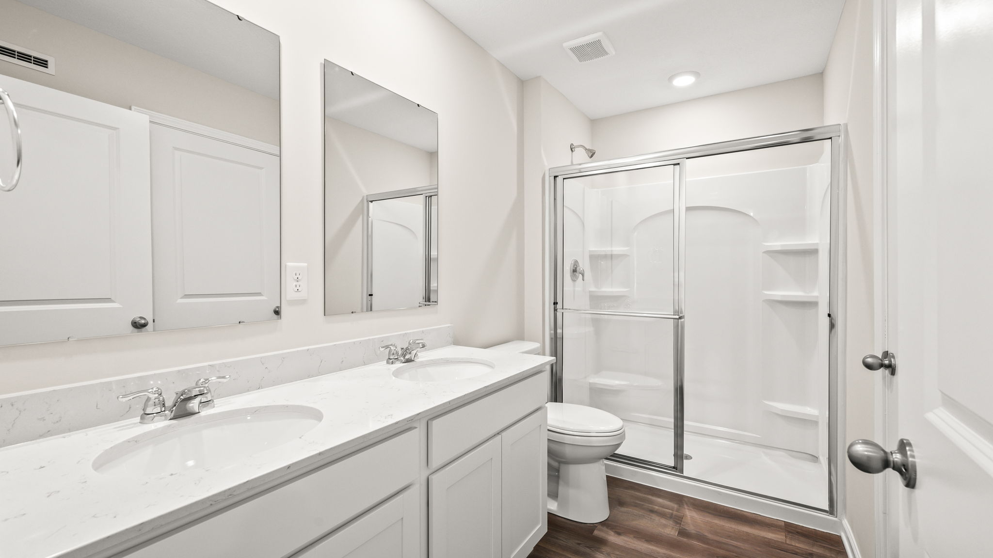 Primary bathroom suite with dual sink mirrors, toilet, and walk-in shower