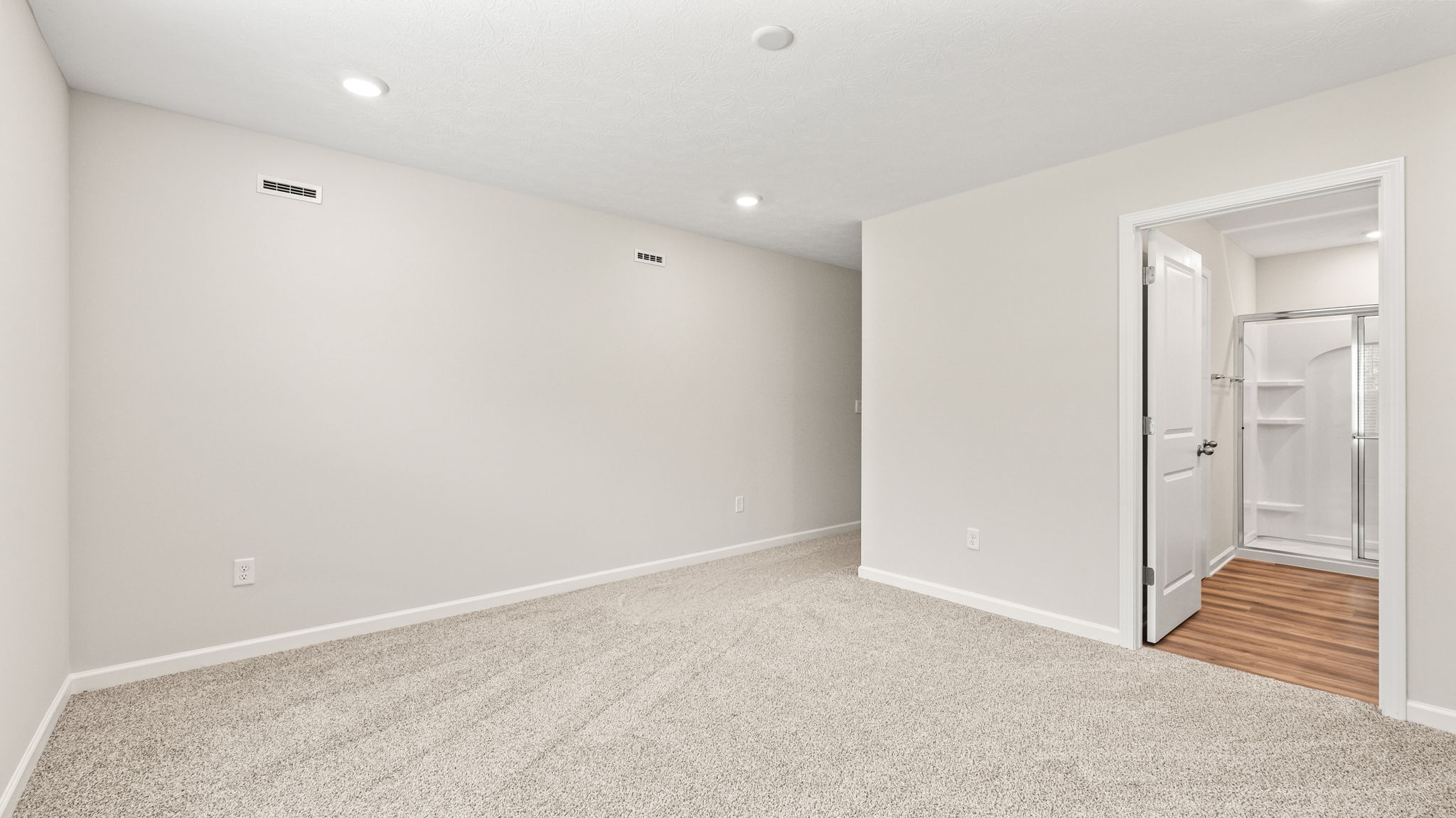 Carpeted primary bedroom with view of primary bathroom suite