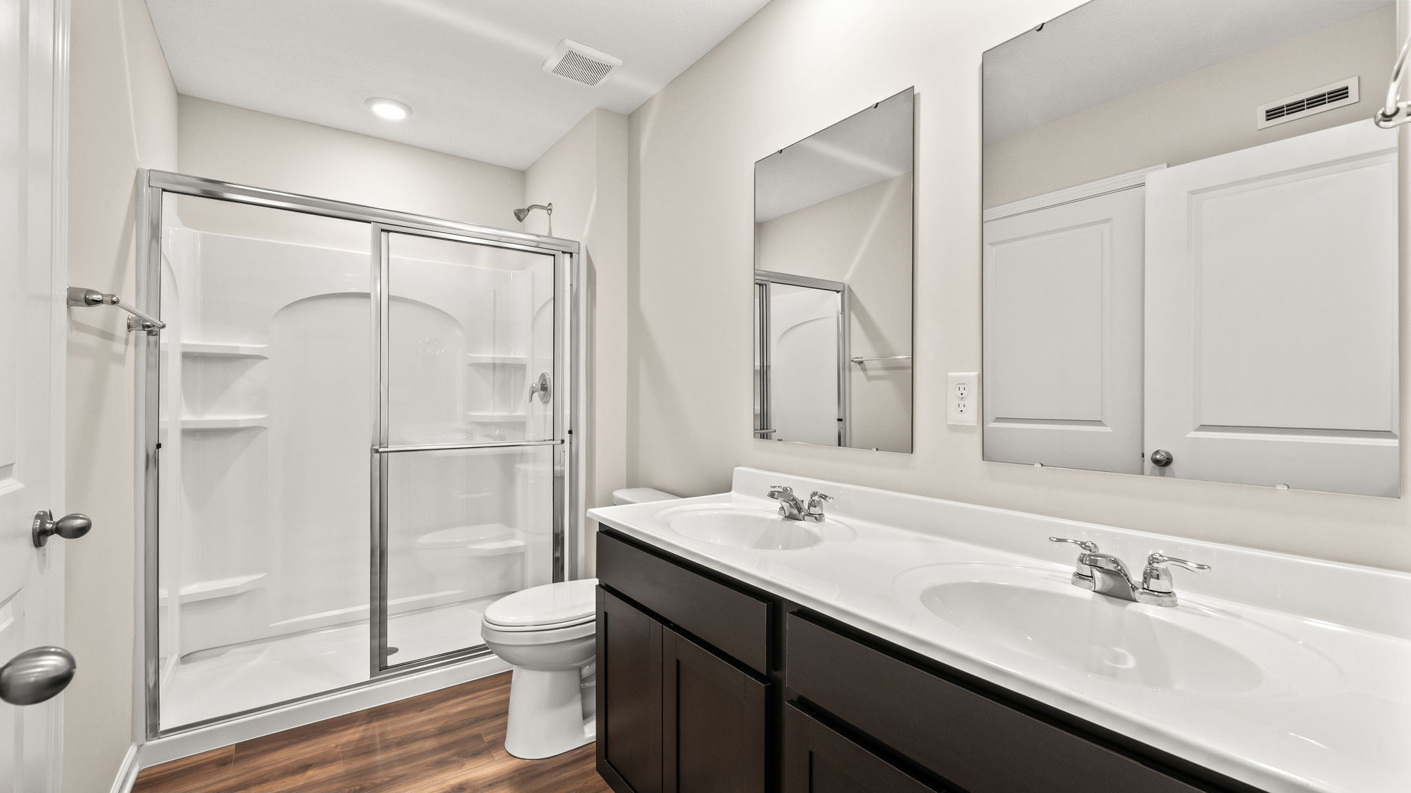 Primary bathroom suite with dual sink vanities and glass door shower