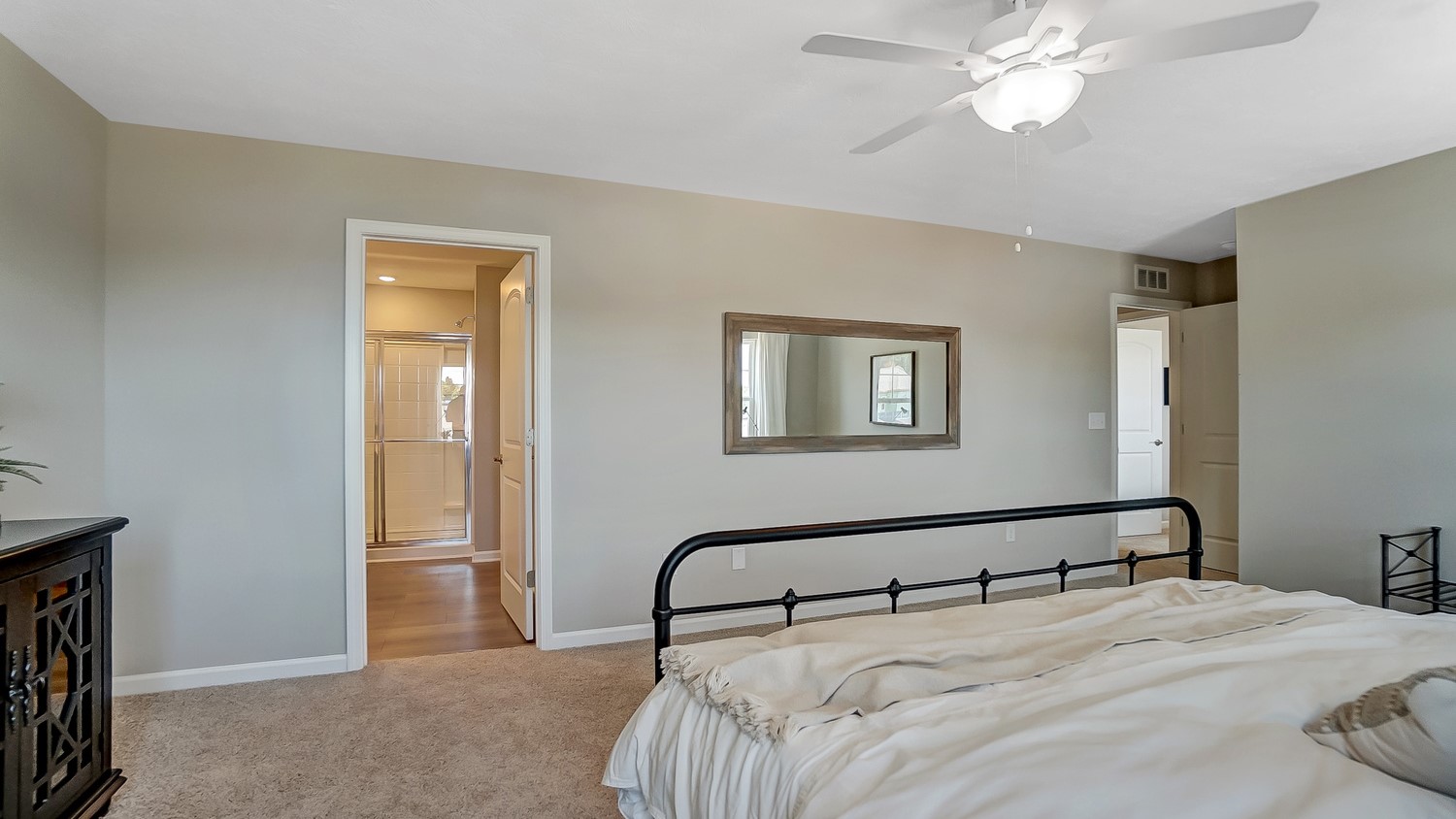 Window view of Primary bedroom with bed and elegant mirrors with view of private bathroom.