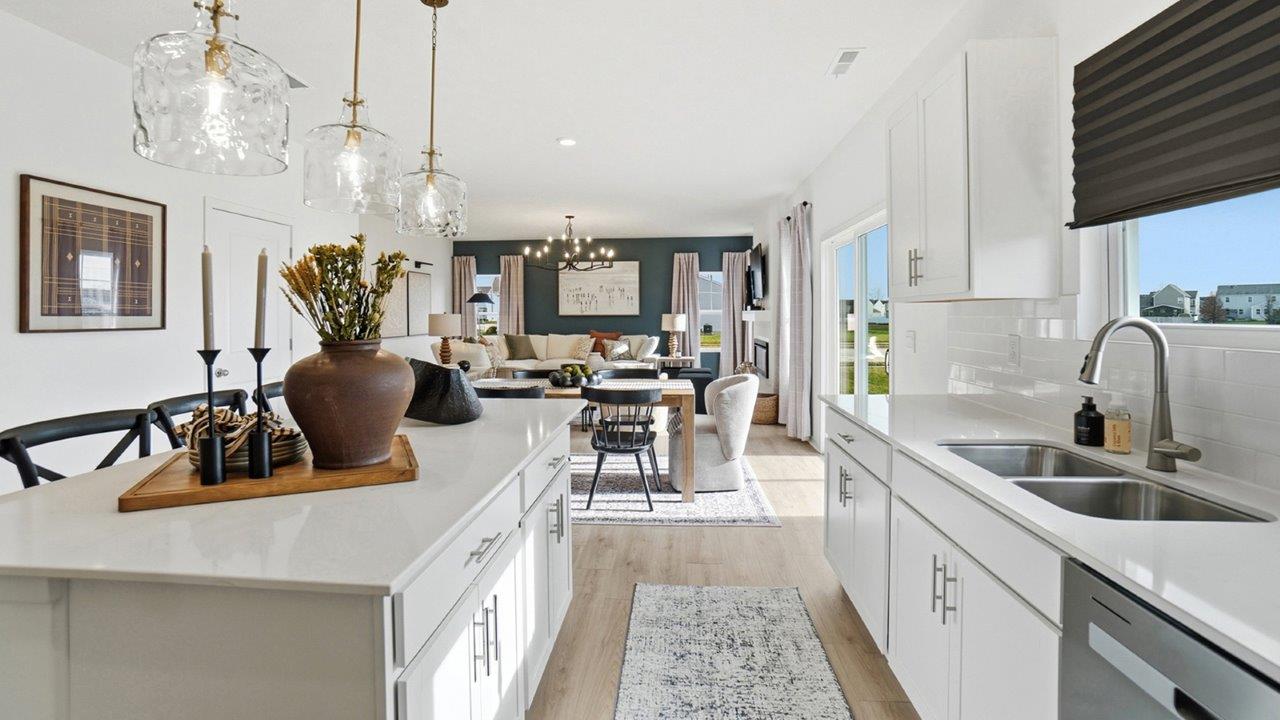 Close view of a double-basin stainless steel kitchen sink beneath a window, with white cabinets and subway tile backsplash.