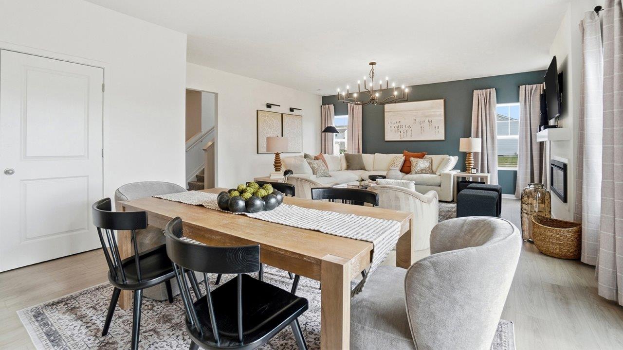 Dining table with mixed black and upholstered chairs overlooking a living room with white sectional, fireplace, and large windows.
