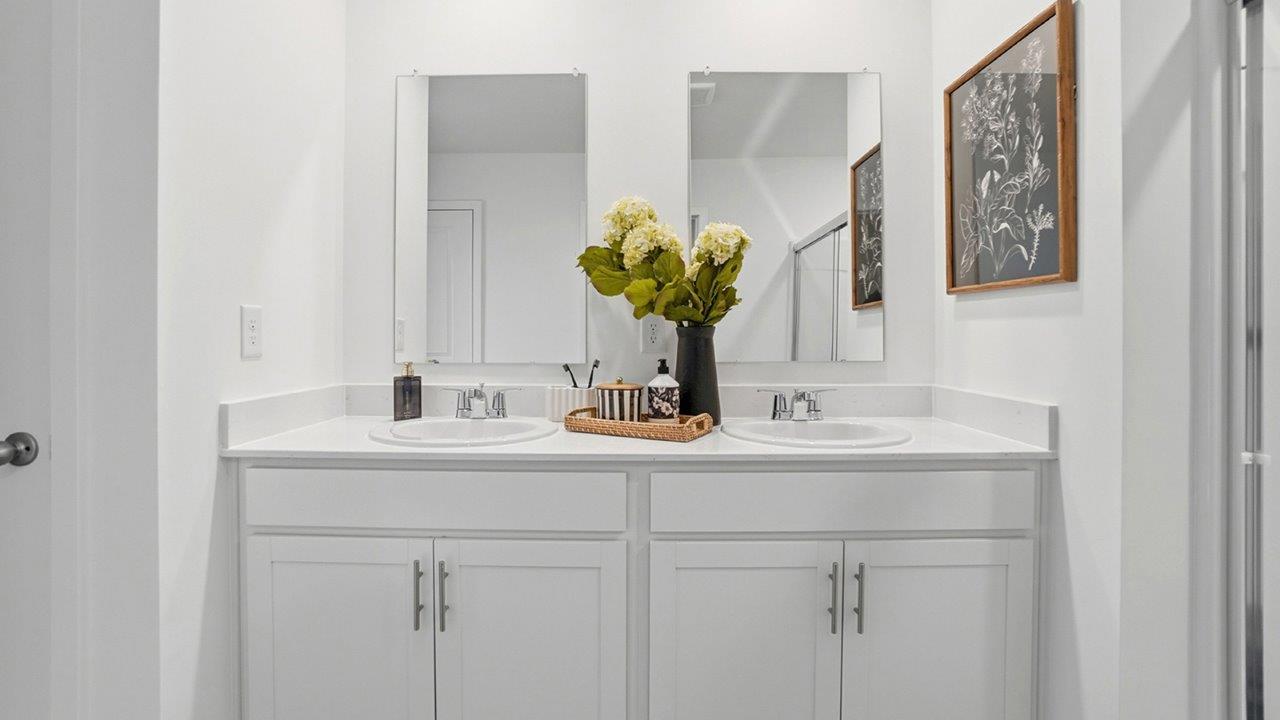 Front view of a white double vanity with two sinks, rectangular mirrors, chrome fixtures, and floral decor.