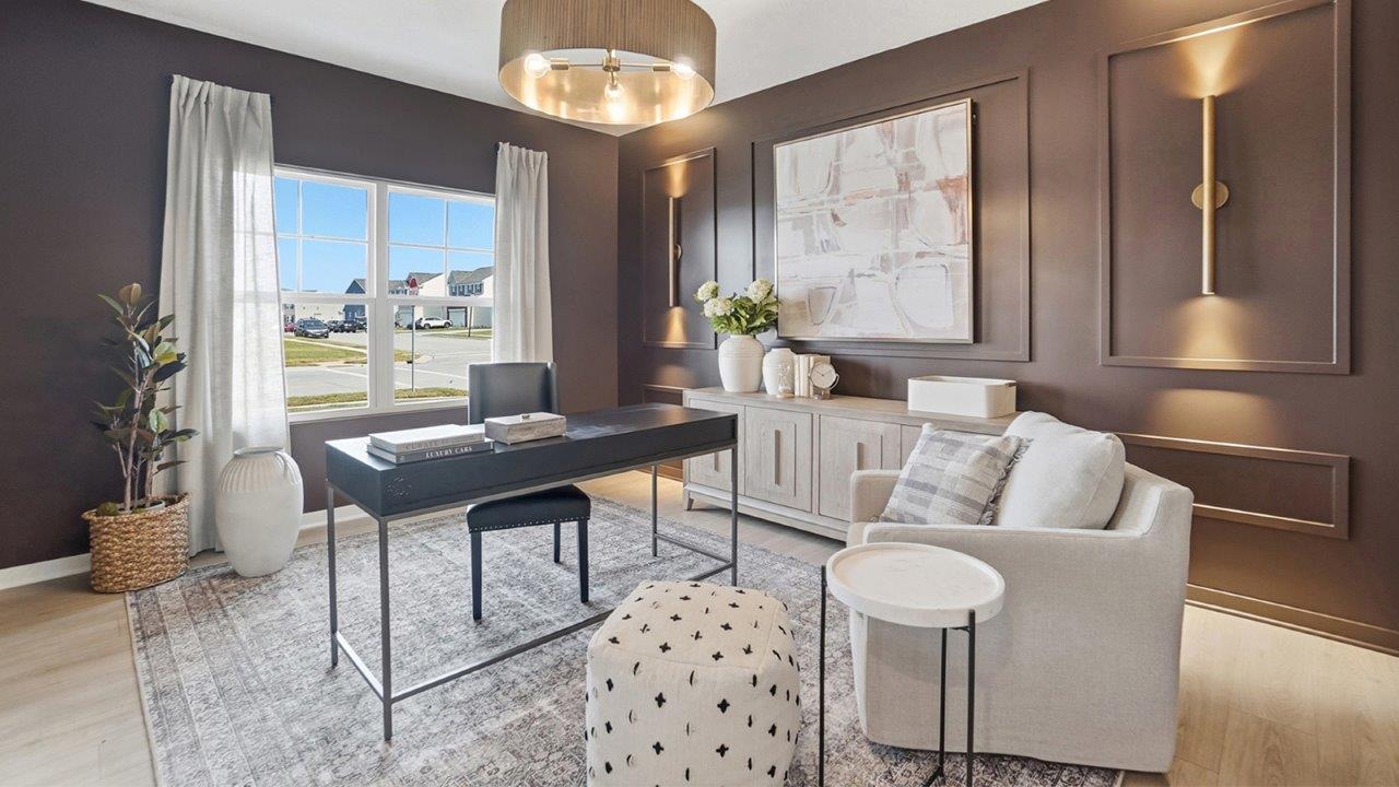 Home office with a dark brown paneled accent wall, black desk, cream chair, area rug, and large window.