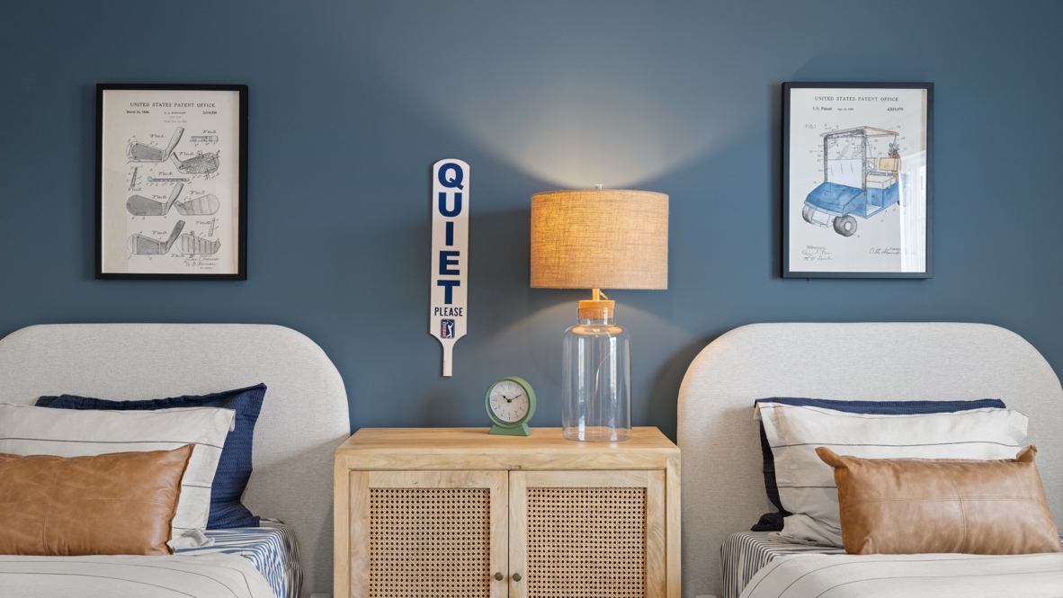 Closeup of two twin sized beds with brown nightstand and golf themed drawings on the wall