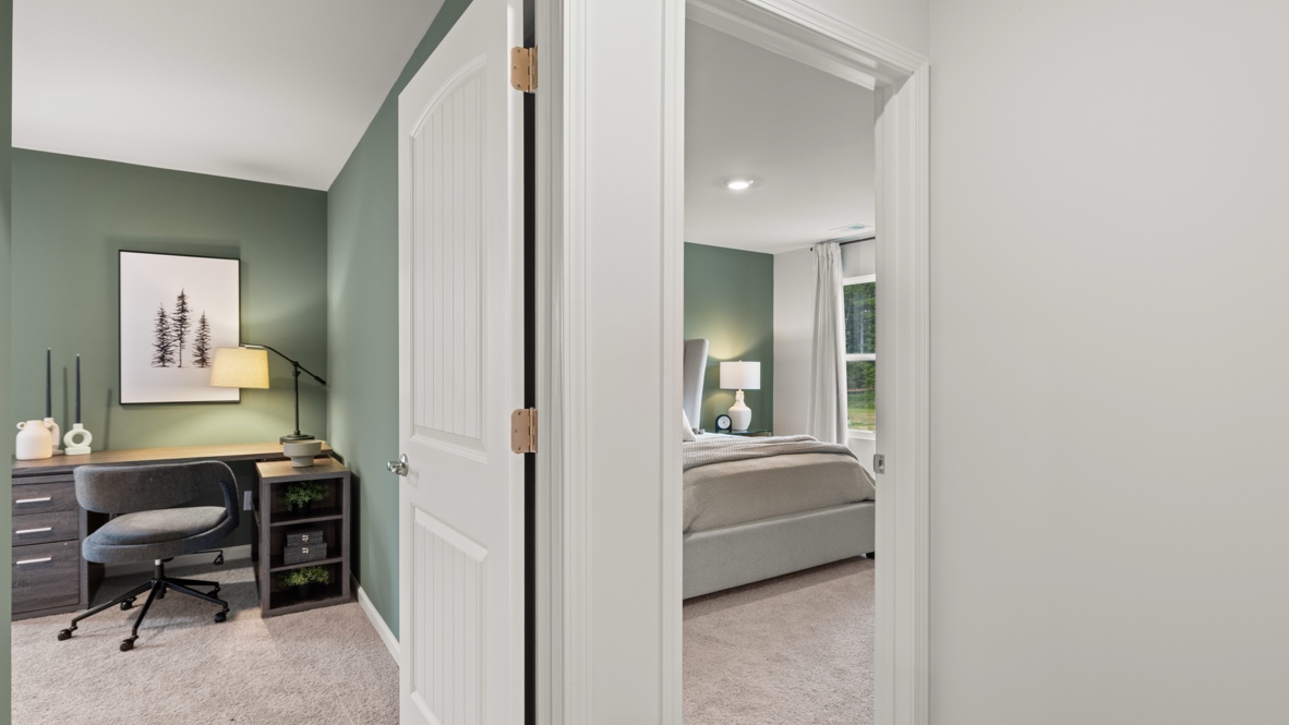Wide image of an office room on the left and bed on the right.