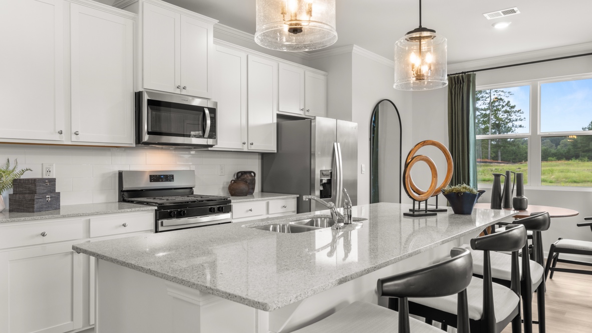 Modern kitchen with bright natural lighting, white cabinetry, stainless steel appliances, and an island with a sink