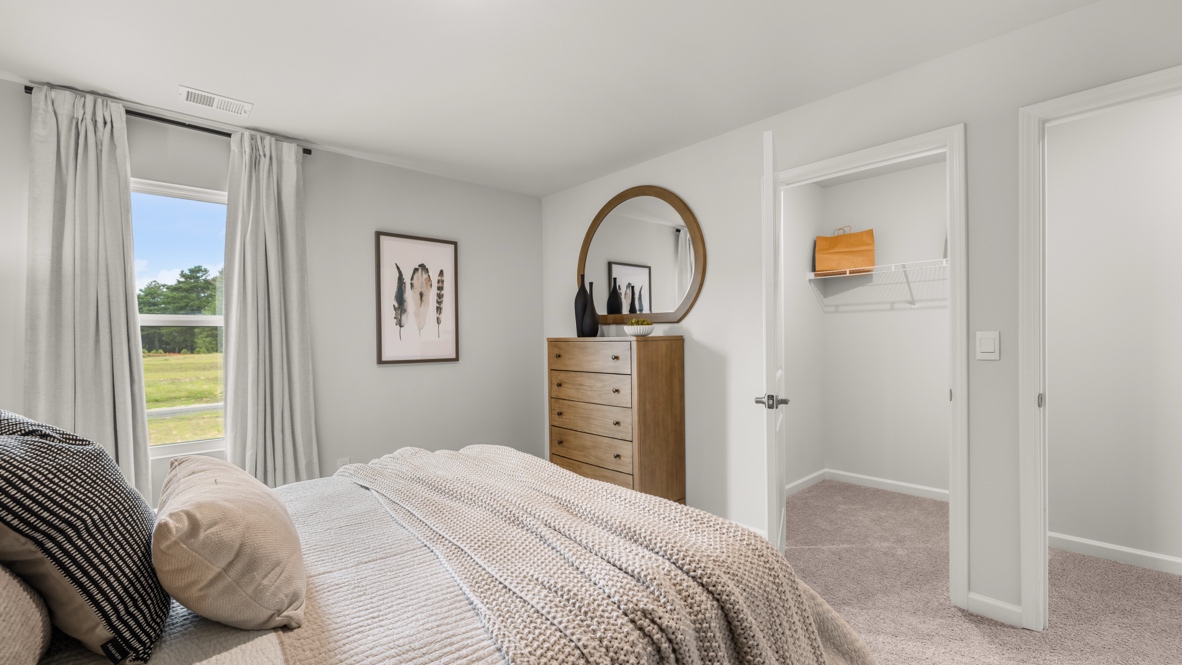 Bedroom 2 from the side of the bed with view of open window, feather art on the wall, queen sized bed, and spacious walk-in closet