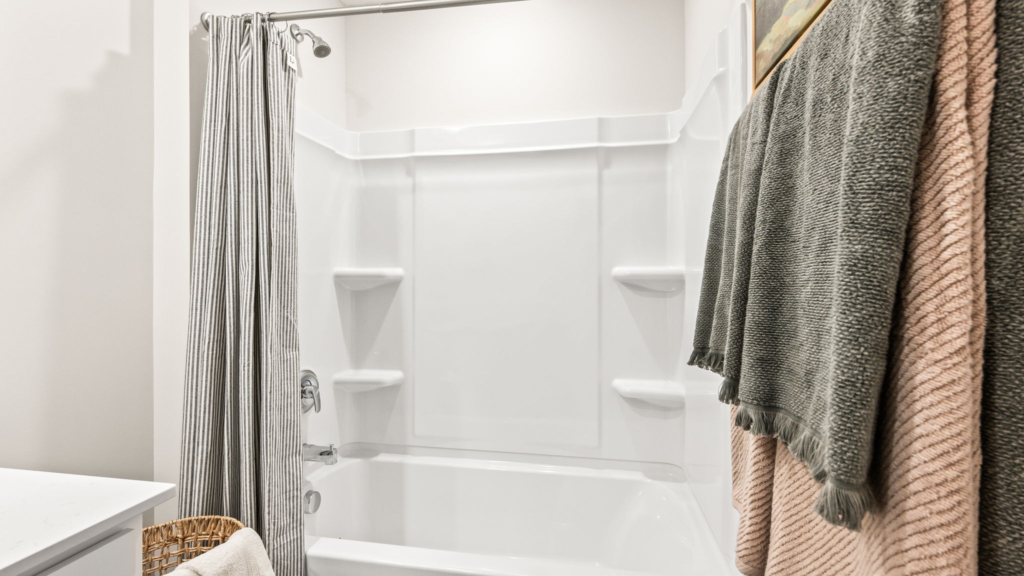 Close view of a white tub-shower combination with built-in corner shelves, chrome fixtures, a gray striped shower curtain, and gray and blush towels.