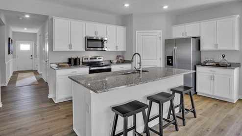 Open concept kitchen with granite countertops, white cabinets, and stainless steel appliances with door to hallway.