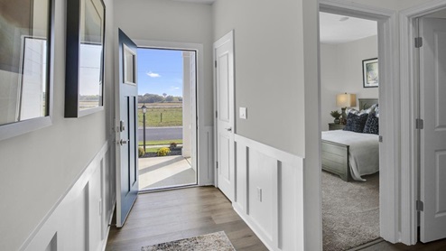 foyer with open door to outside with bedroom bed in view.