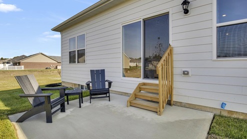 small back concrete patio with adirondacks and large sliding door.
