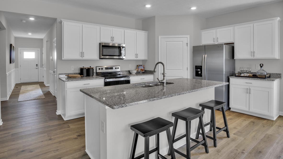 Open concept kitchen with granite countertops, white cabinets, and stainless steel appliances with door to hallway.