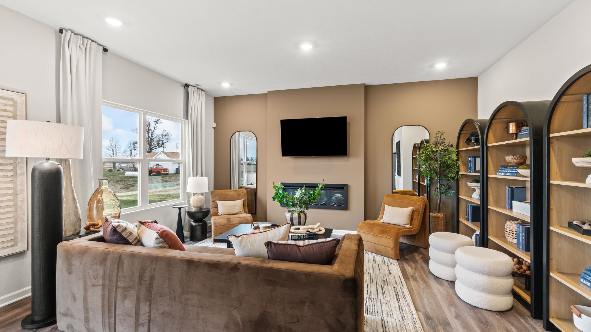 Modern living room with brown and blue tones, cloth couches, bookshelves, and plants.