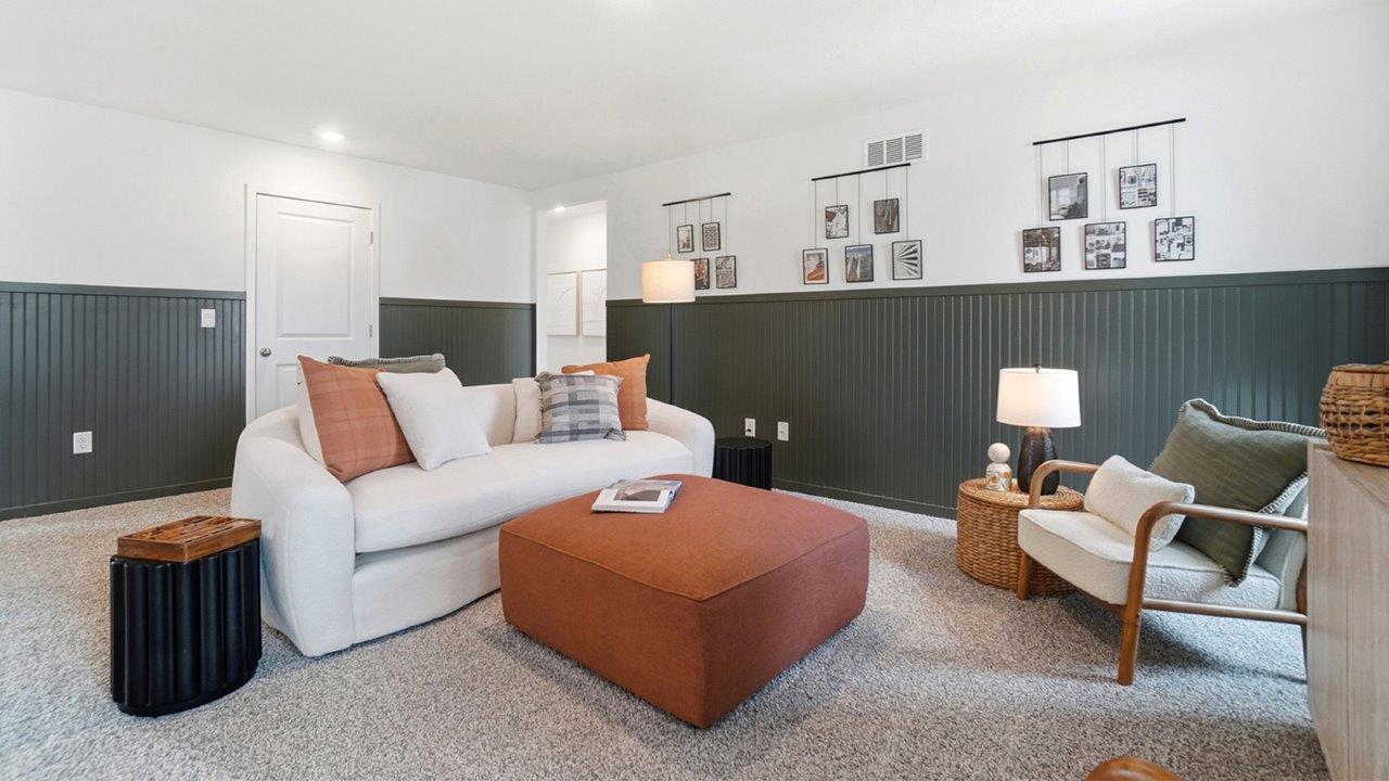 Loft with a white sofa, orange ottoman, accent chair, gallery wall, and dark green wainscoting.
