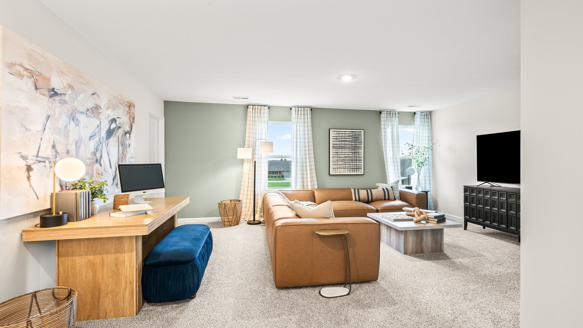 Upstairs bonus room with a tan sectional, television on a dark media console, a wood desk with computer, blue bench, large abstract wall art, and carpeted flooring.