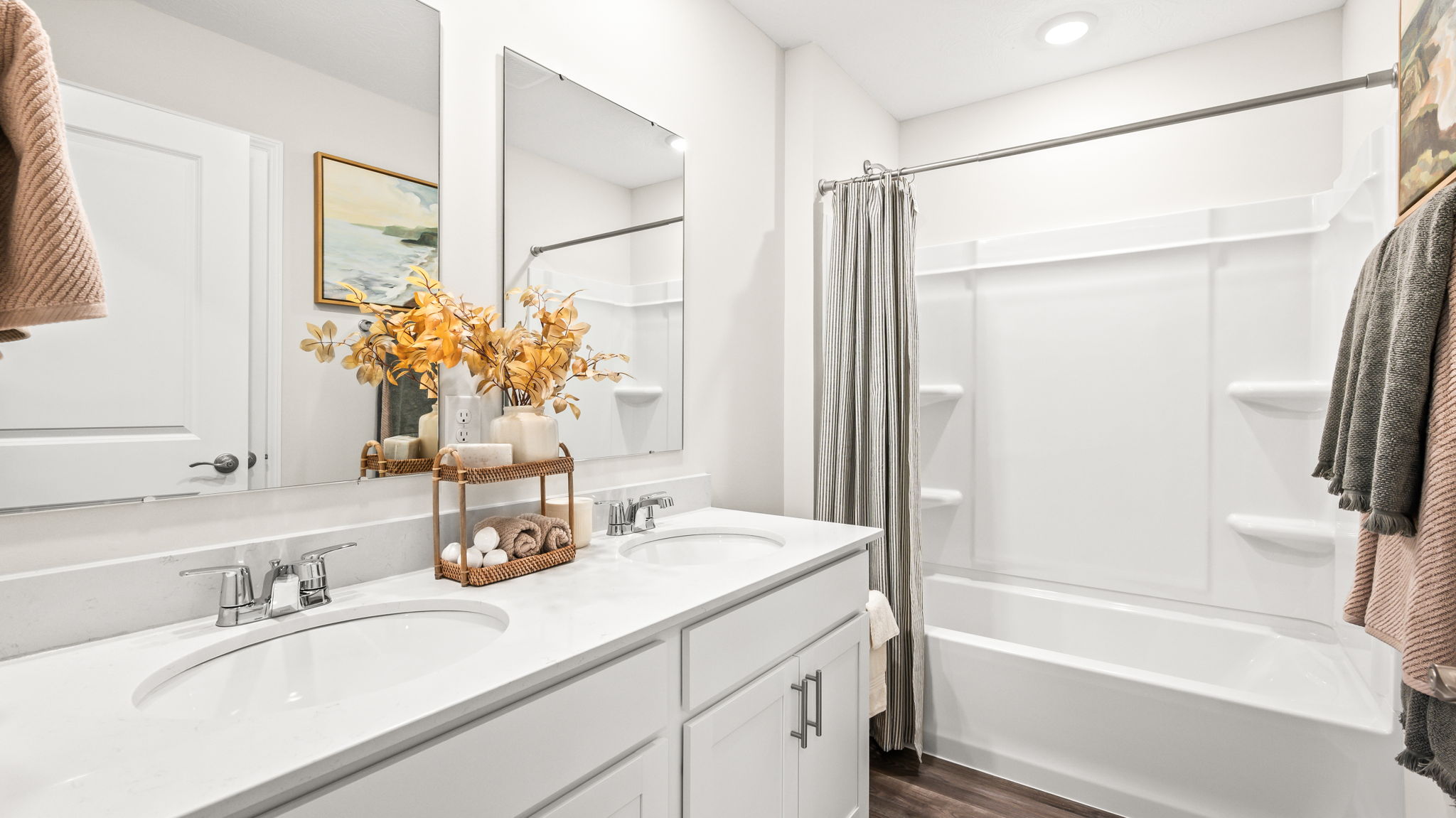 Bathroom with a white vanity and sink, large wall mirror, chrome fixtures, floral arrangement, and a tub-shower combination with a gray curtain and built-in shelves.