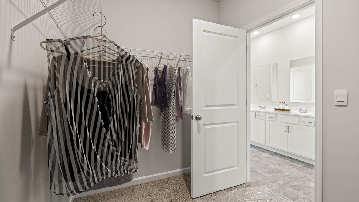 Walkin closet with clothes and view of dual vanity sinks in bathroom.