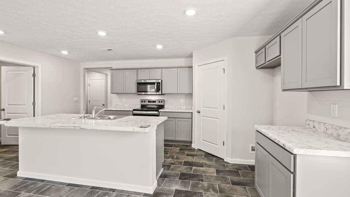 Quarter perspective of kitchen with laminate countertops, grey cabinetry, stove and microwave, and door to pantry