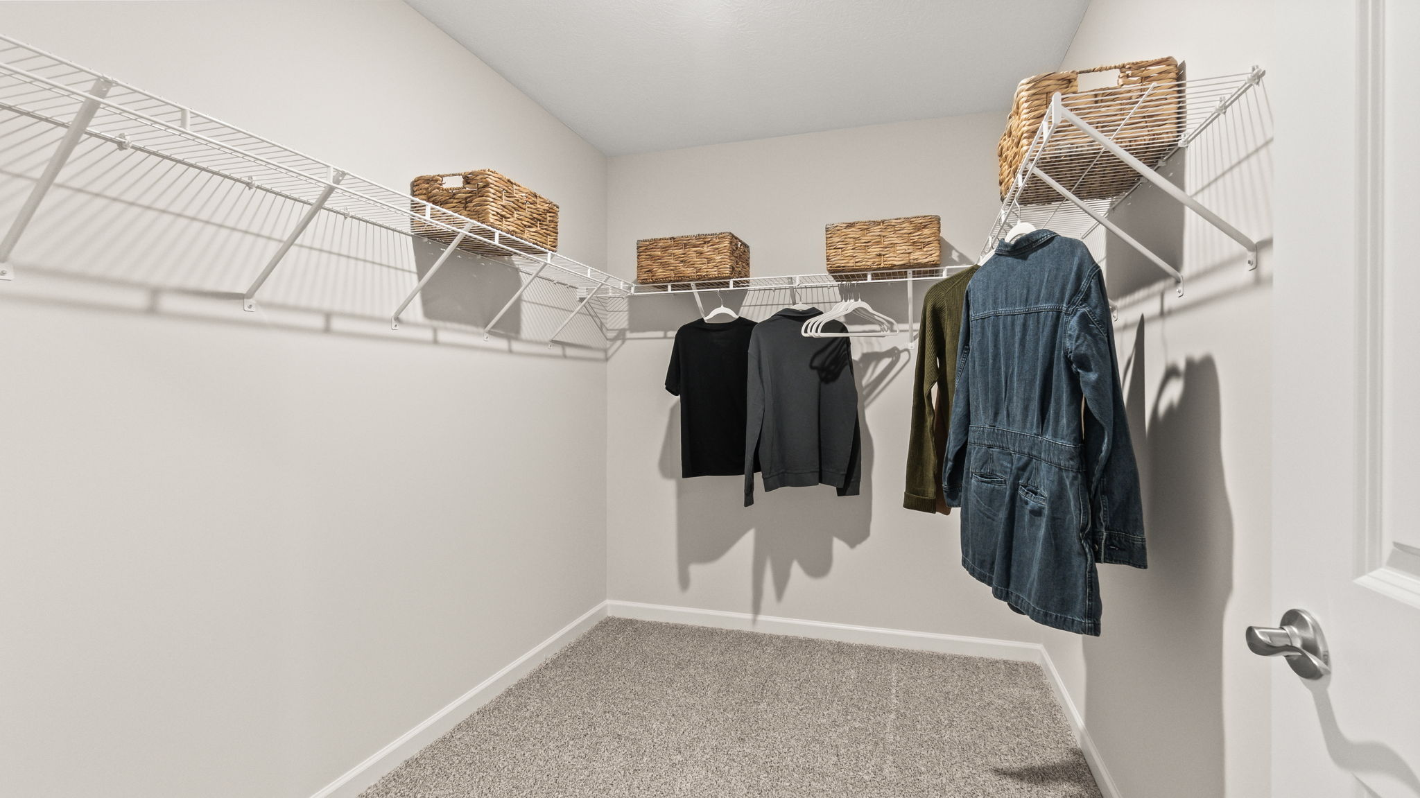 Carpeted walk-in closet, wire shelving, and cool-color clothes.