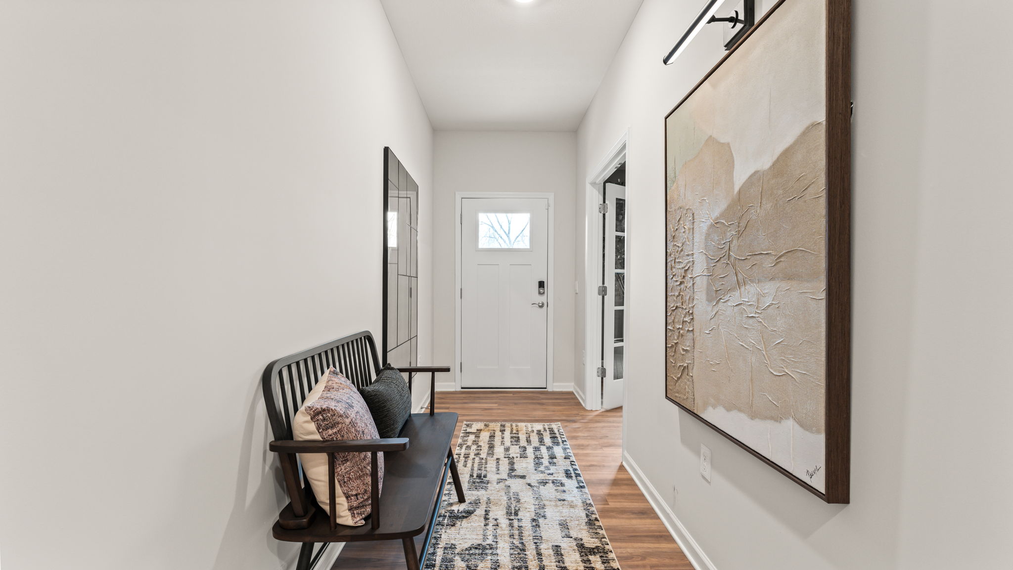 Hallway leading to the front door with abstract art on the wall and a brown bench with pillows