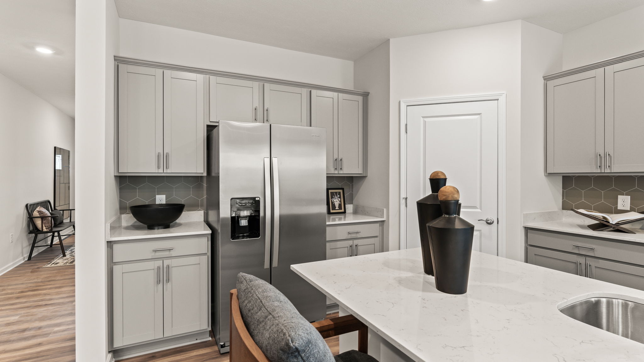 Stainless steel fridge between gray cabinetry next to walk-in pantry door