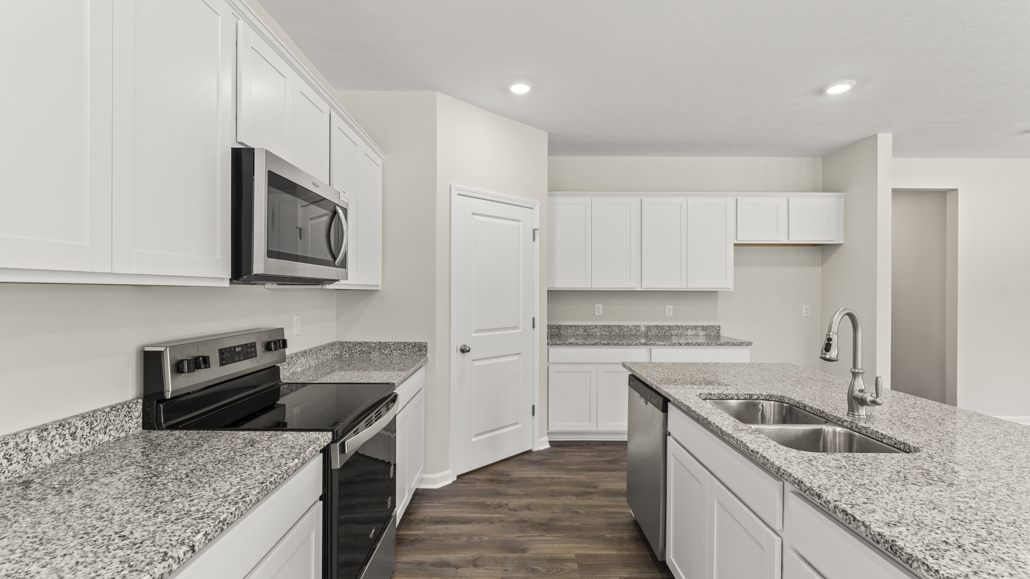 Side view of kitchen granite countertops, oven range, microwave, and white cabinetry