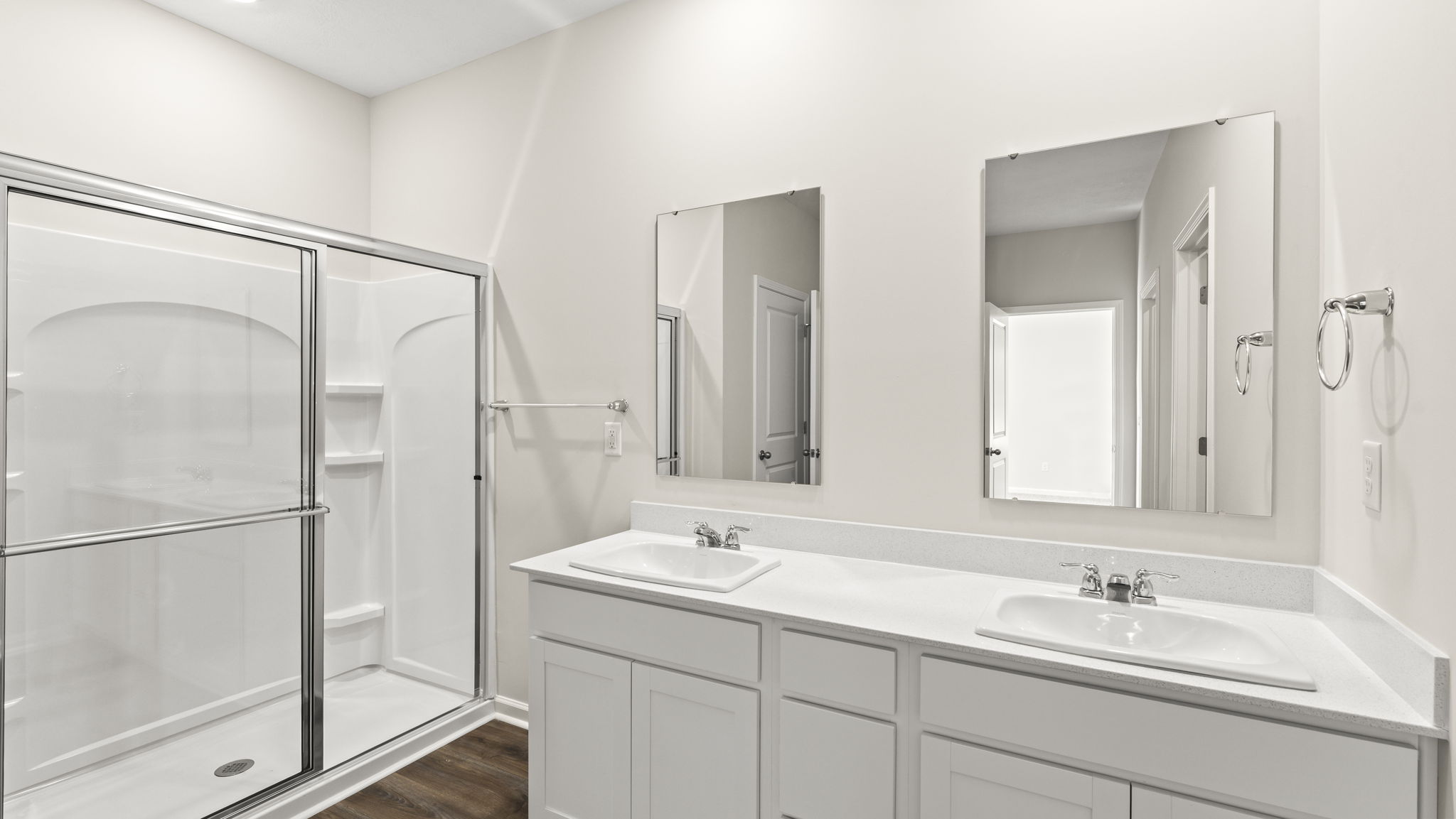 Primary bathroom with sliding glass shower door, dual sink vanity, and mirrors