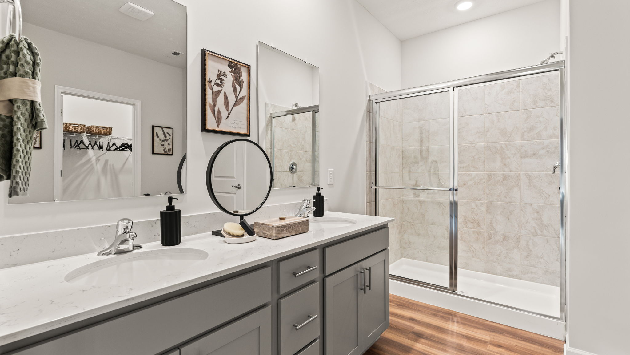 Primary bathroom with gray cabinets, quartz countertops, double bowl vanity with two mirrors, and beautiful walk-in shower
