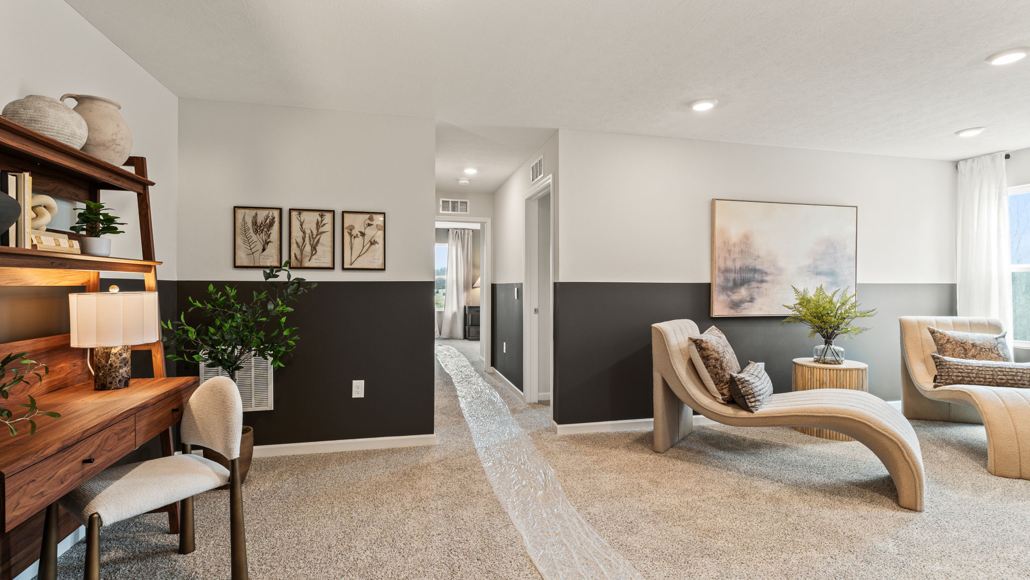 Upstairs loft arranged in a cozy lounge room with wooden desk, two tone black & white walls, and long comfortable white cloth chairs
