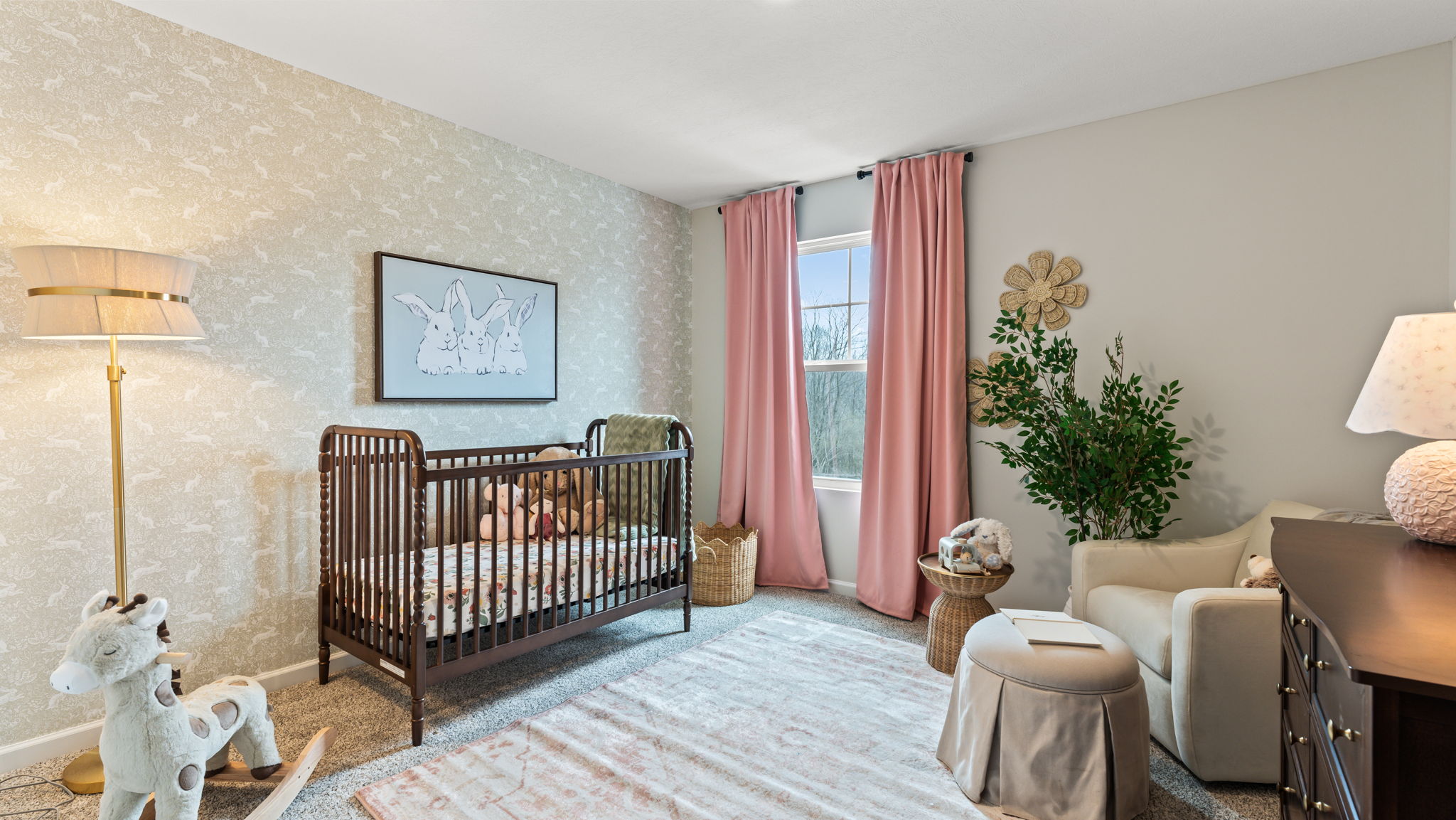 Bedroom arranged as a nursery with wooden crib, rocking horse, pastel pink drapes, and soft inviting carpets and couches.