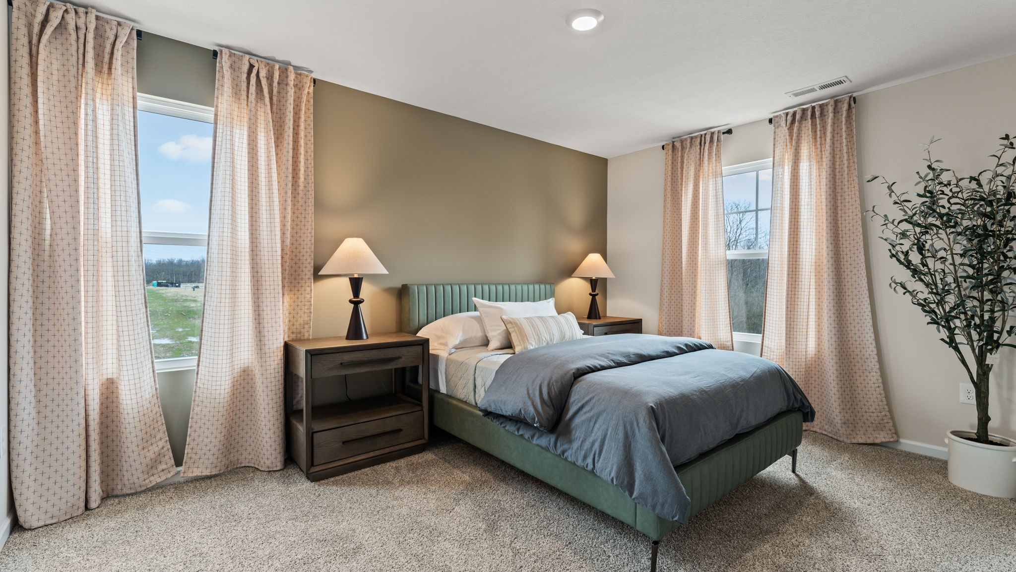Three-quarter view of bedroom with green bed frame, pastel curtains, and a blen of warm lighting from the lamps and clean natural lighting