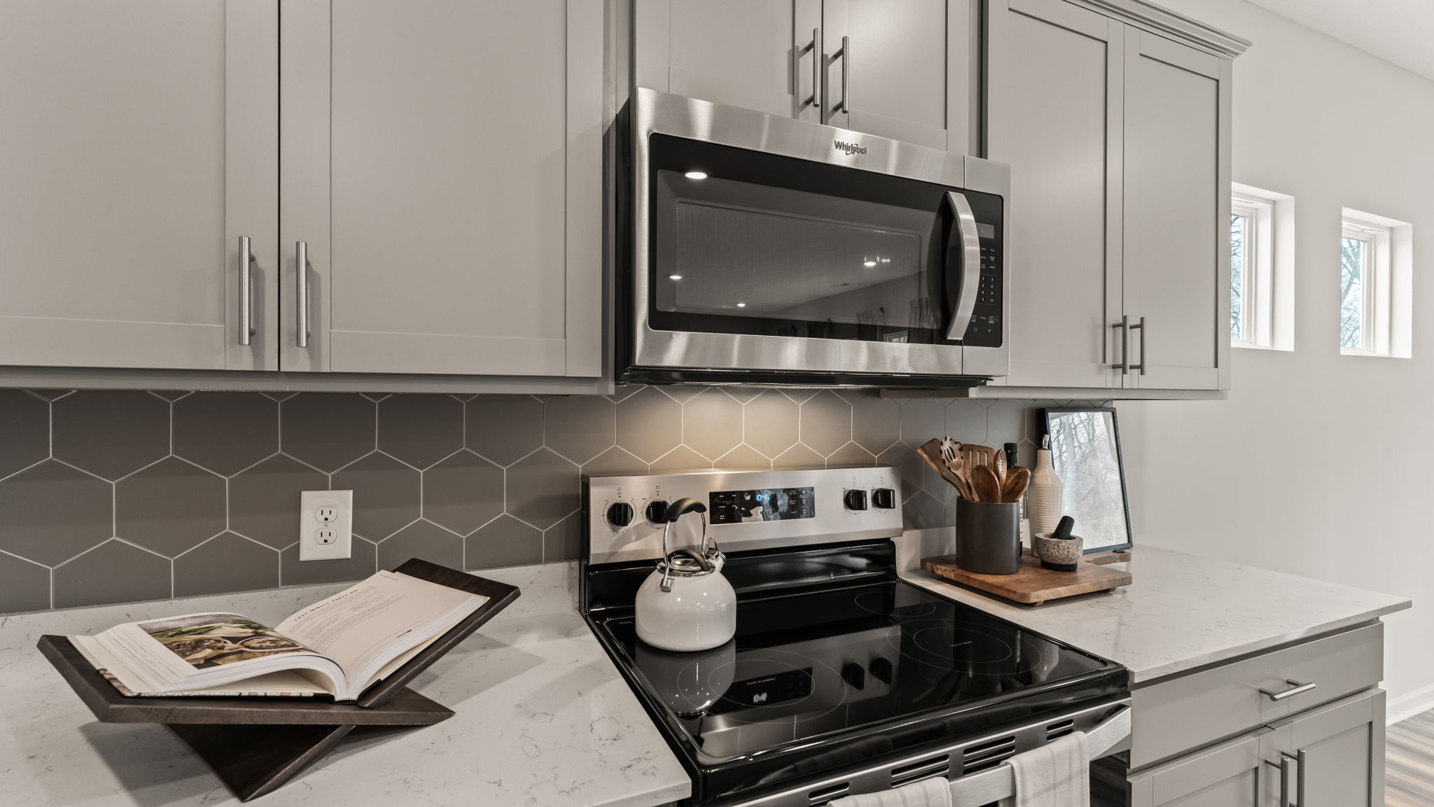 Closeup of stainless steel appliances between gray cabinetry, and technical hexagonal backsplash