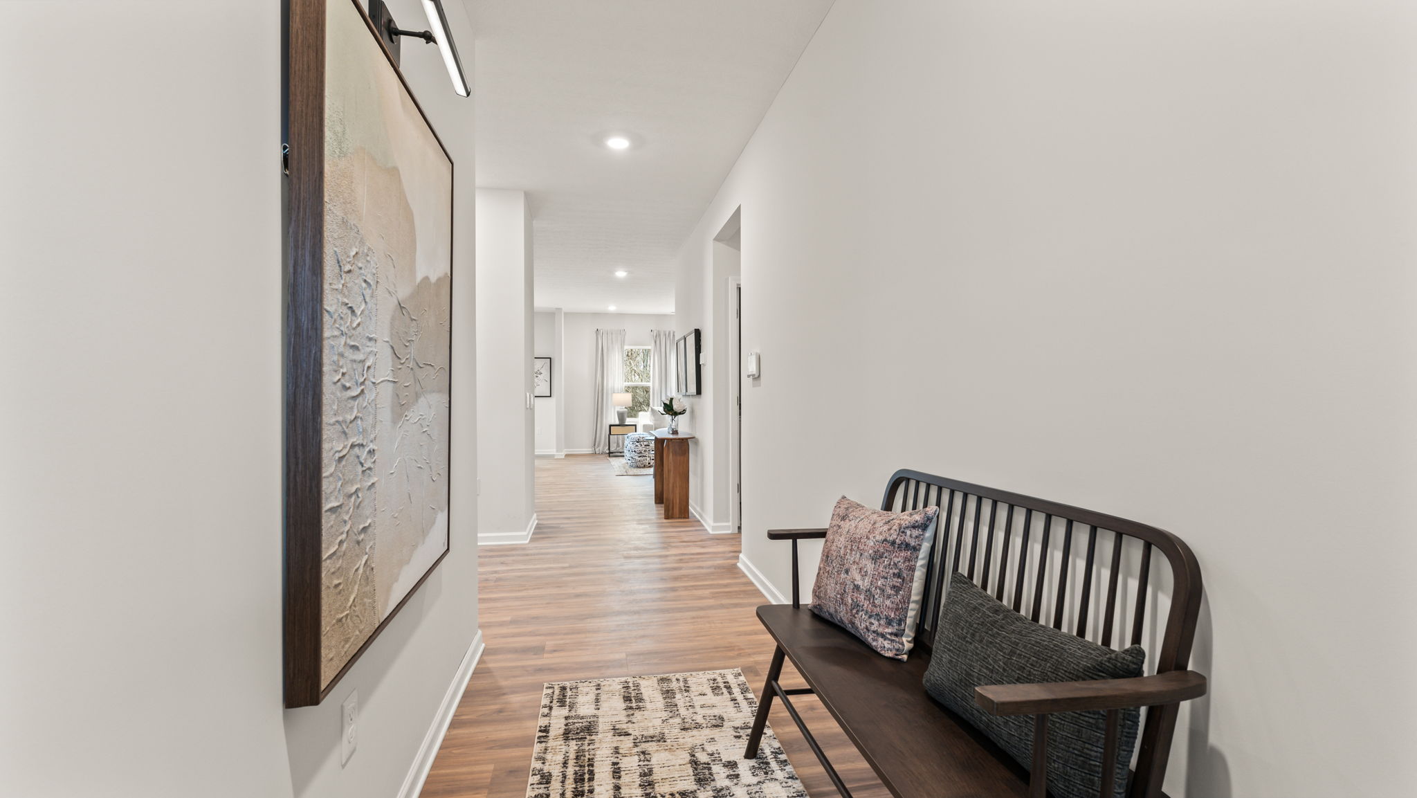 Hallway into the great room with abstract art on the wall and a brown bench with pillows