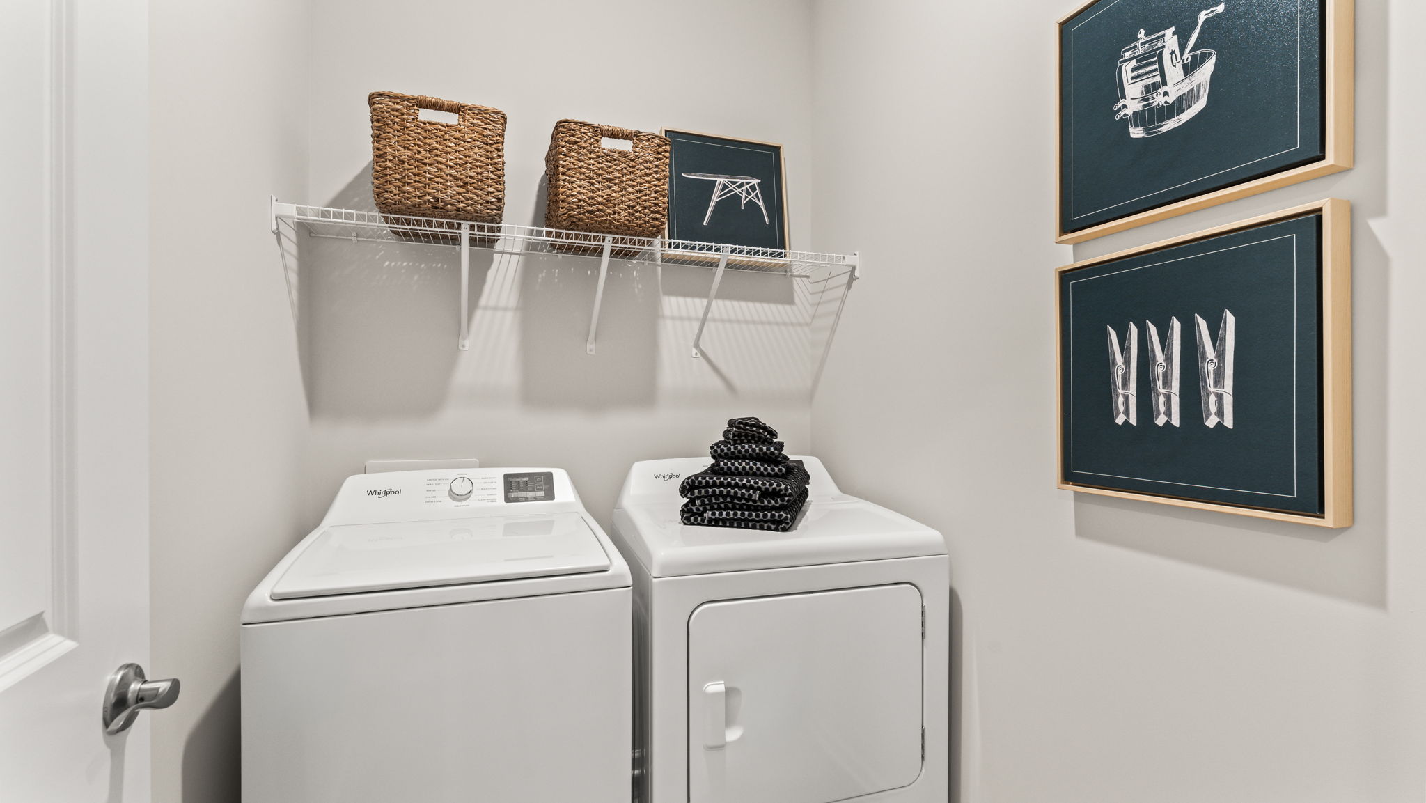 Laundry area with washer/dryer and wire rack shelving holding baskets and art piece