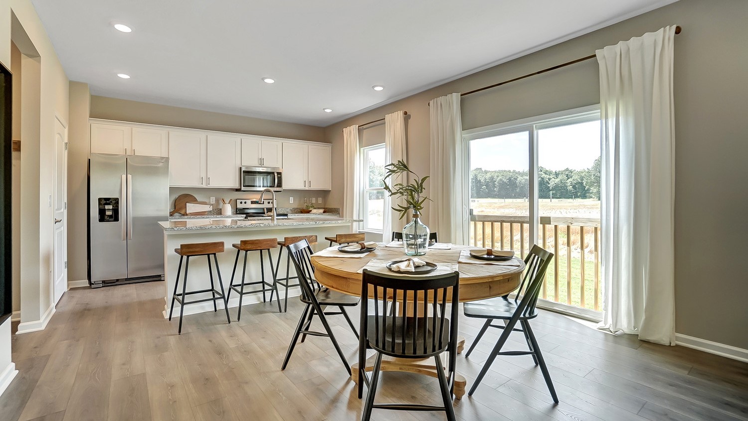 Modern Open Concept view of the great room with wood table white cabinets and stainless steel appliances.