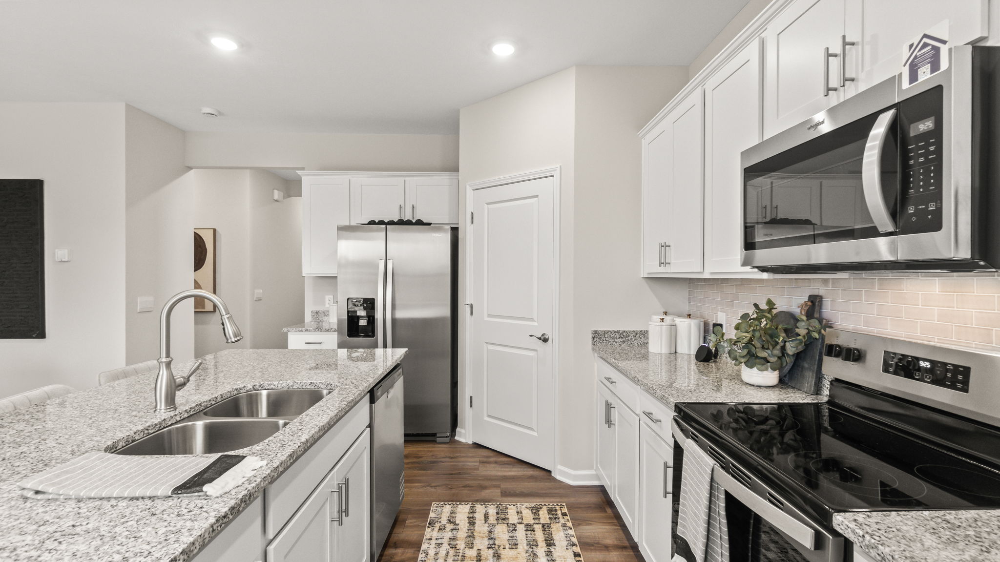 Side view of kitchen with island/sink on the left, fridge and pantry in the center, and appliances with cabinetry on right.
